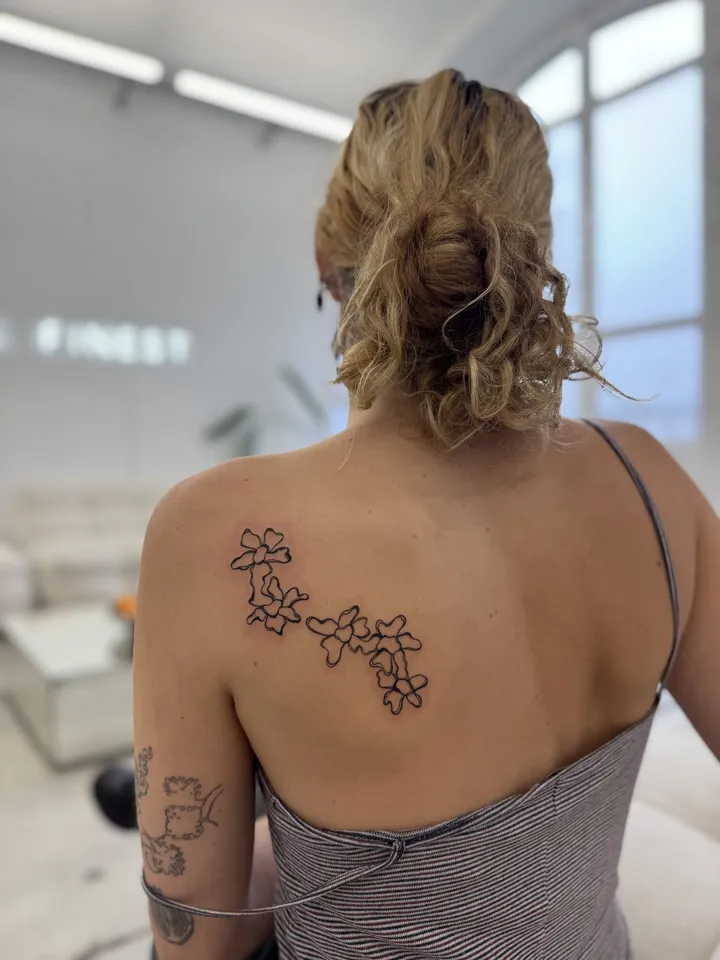 Fine-line narcissus trail across a shoulder blade