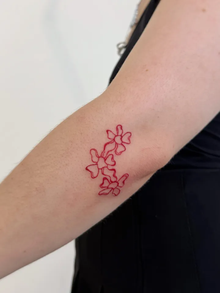 Fine-line florals tattooed in red on the inner forearm