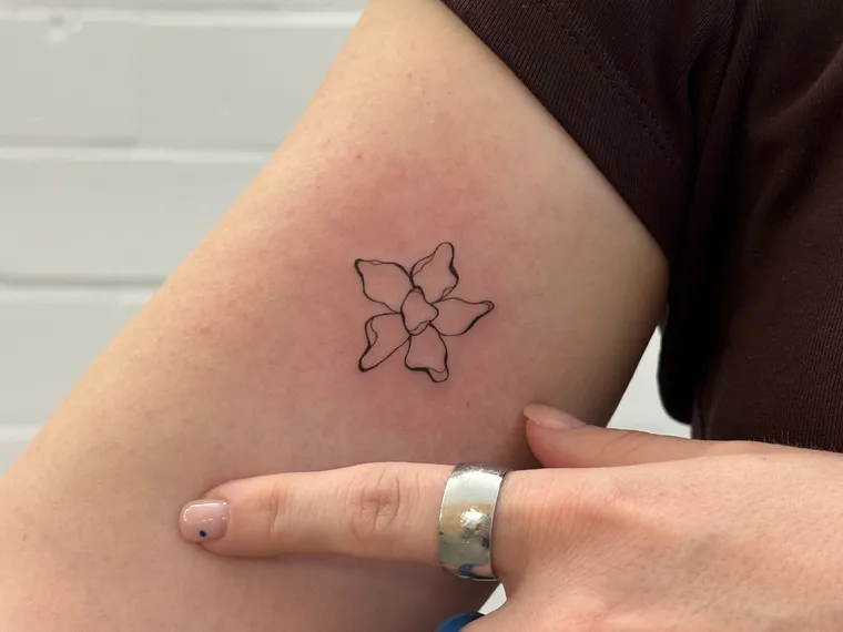 A client pointing at her finished fine-line blossom, just above the elbow